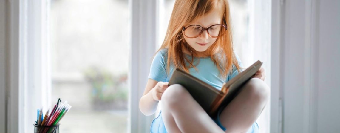 A young ballet student in her leotard, tights, and ballet slippers reads books about dance class