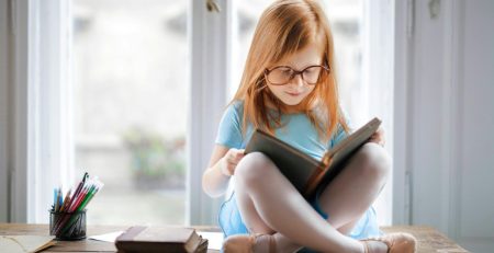 A young ballet student in her leotard, tights, and ballet slippers reads books about dance class
