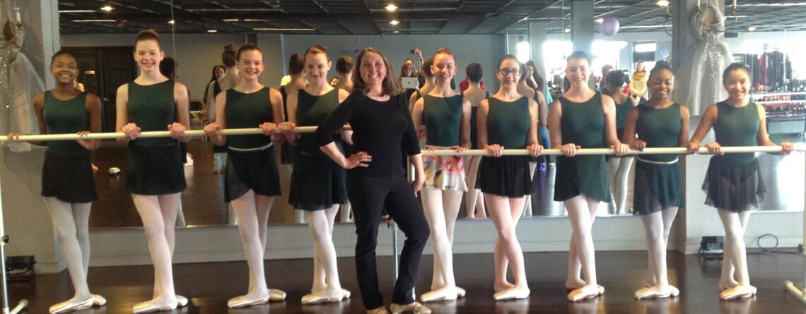 Ballet dancers at The Link School of the Arts stand with their dance teacher at the ballet barre at their local dance studio