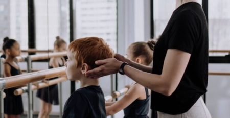 A dance teacher corrects a young boy in dance class at the ballet barre