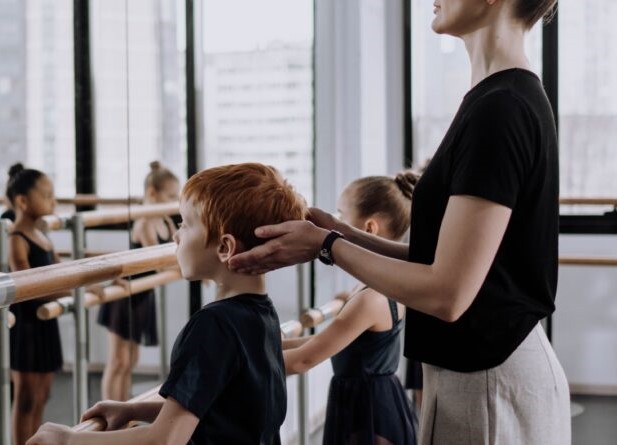 A dance teacher corrects a young boy in dance class at the ballet barre